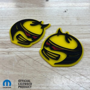 May include: Two yellow and black car emblems with a red stripe. The emblems are shaped like a stylised head with horns. The text "OFFICIAL LICENSED PRODUCT" is visible below the emblems.