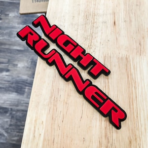 May include: Red and black plastic emblem with the words "NIGHT RUNNER" in a bold, stylized font.
