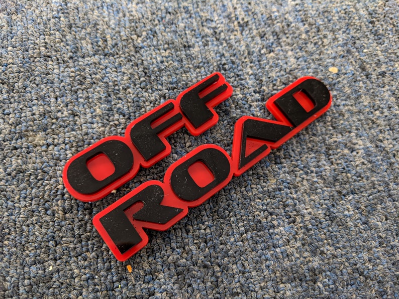 May include: Red plastic emblem with black lettering that reads "OFF ROAD".