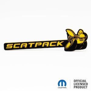 May include: Black and yellow Scat Pack emblem featuring a cartoon bee design. The emblem is a long rectangle with the words "SCAT PACK" in yellow lettering on a black background. The bee is on the right side of the emblem and is facing left. The bee is wearing a yellow helmet and has a yellow stinger.