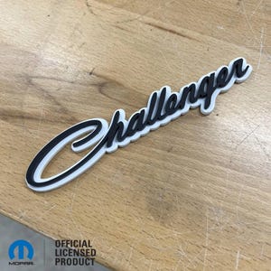May include: A black and white 3D printed "Challenger" emblem with a white background and black lettering. The emblem is an officially licensed product.