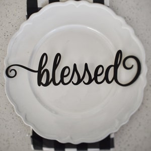 May include: A white plate with a black, cursive word "blessed" on it. The plate is on top of a black and white checkered napkin.