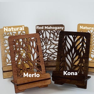 May include: Four wooden phone stands with a leaf design. The stands are in the colors natural, red mahogany, merlo, and kona.