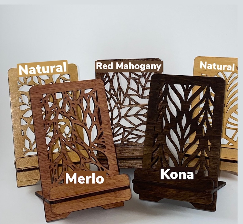 May include: Four wooden phone stands with a leaf design. The stands are in the colors natural, red mahogany, merlo, and kona.