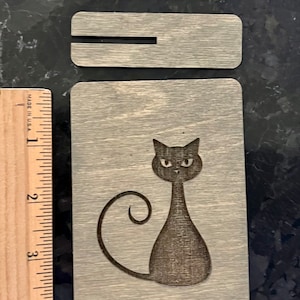 May include: A wooden coaster with a black cat design. The cat is sitting with its tail curled around its body. The coaster is made of wood with a light gray finish.