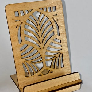 May include: A wooden phone stand with a decorative cutout design. The stand is made of light brown wood and has a simple, modern design.