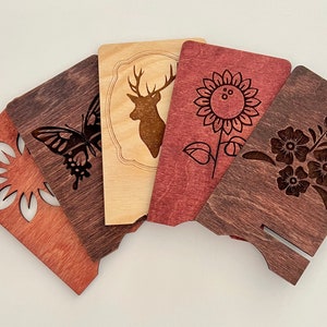 May include: Five wooden coasters with laser-cut designs. The coasters feature a butterfly, a deer, a sunflower, a floral design, and a simple geometric design. The coasters are stained in shades of brown and red.