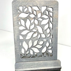 May include: Weathered grey wooden phone stand with a leaf design. The stand has a slot for holding a phone.