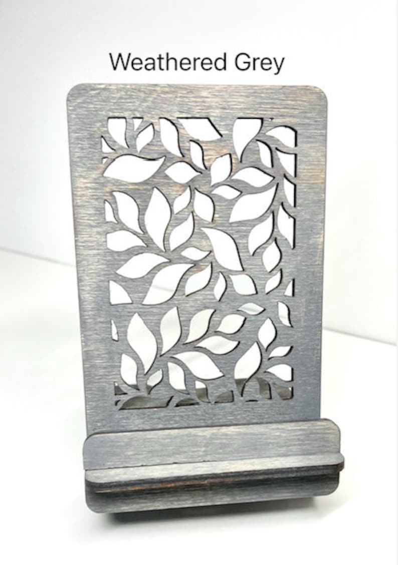 May include: Weathered grey wooden phone stand with a leaf design. The stand has a slot for holding a phone.