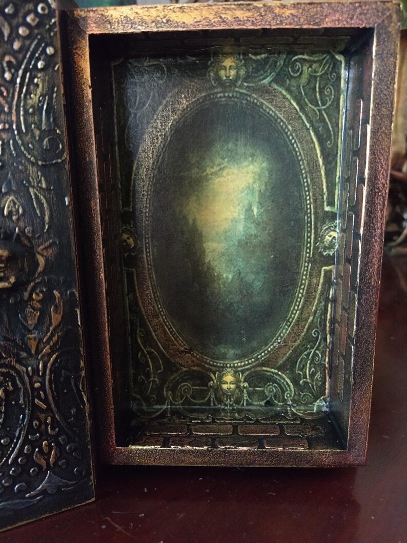 May include: An ornate wooden box with a hinged lid. The inside of the box is decorated with a green and gold oval frame with a faded image inside. The box is closed and the lid is visible.