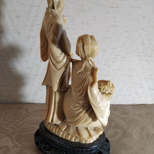 May include: A cream-colored ceramic figurine of a couple standing on a black base. The woman is holding a bouquet of flowers. The figurine is in a traditional Chinese style.