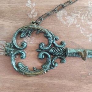May include: A decorative key-shaped wall hook with a teal and gold finish. The hook is attached to a chain and has a decorative design.