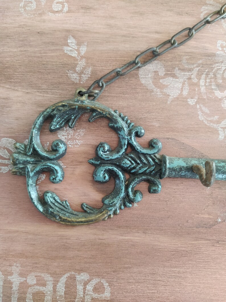 May include: A decorative key-shaped wall hook with a teal and gold finish. The hook is attached to a chain and has a decorative design.