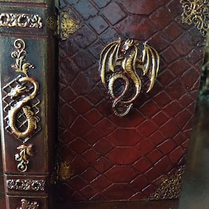 May include: A red leather-bound book with a gold dragon design on the cover. The book is closed and has a decorative spine with gold accents.