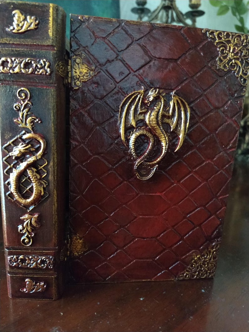May include: A red leather-bound book with a gold dragon design on the cover. The book is closed and has a decorative spine with gold accents.