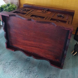 Op de afbeelding: Een donkerhouten juwelendoos met ingewikkelde houtsnijwerk en een scharnierend deksel. De doos heeft een decoratief ontwerp aan de voor- en zijkanten.