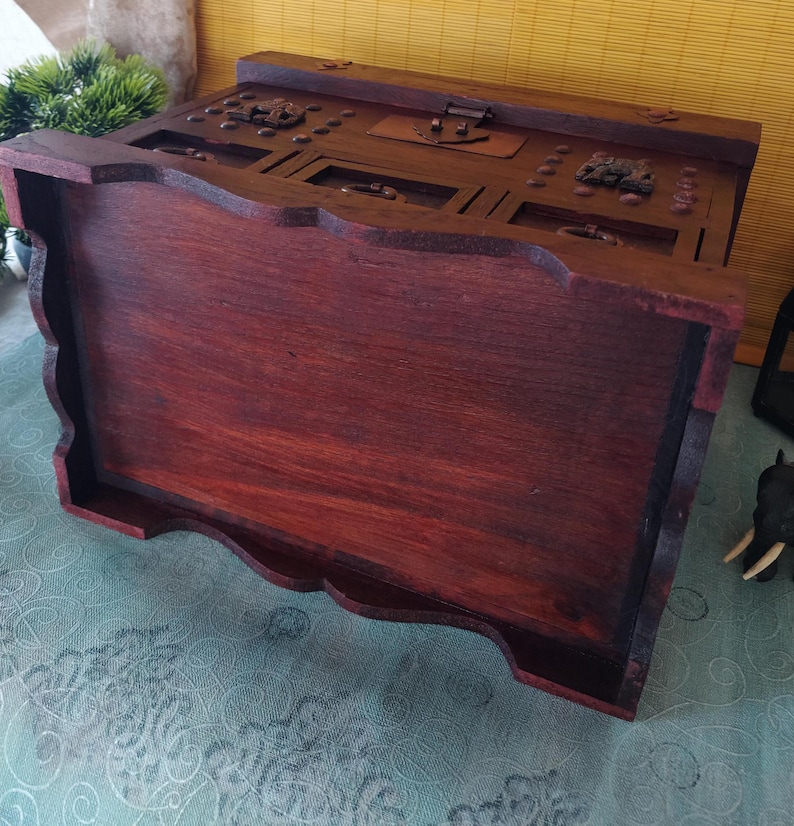 Op de afbeelding: Een donkerhouten juwelendoos met ingewikkelde houtsnijwerk en een scharnierend deksel. De doos heeft een decoratief ontwerp aan de voor- en zijkanten.