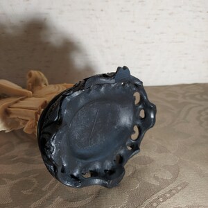 May include: A black carved wooden base with intricate details. The base has a circular shape with a raised edge and a small hole in the center.