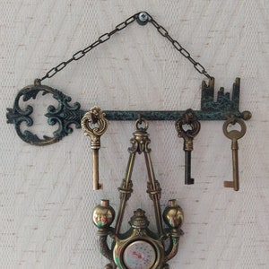 May include: A decorative key-shaped wall hanger with a chain, three keys, and a hanging thermometer with a brass finish.