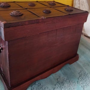 Op de afbeelding: Een donkerbruine houten kist met een scharnierend deksel. Het deksel heeft een decoratief ontwerp met metalen accenten en een textuur.