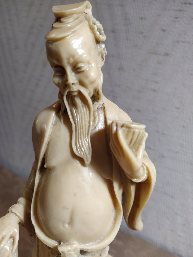 May include: A white ceramic figurine of a man with a long beard and a hat. He is wearing a long robe and holding a scroll in his hand.