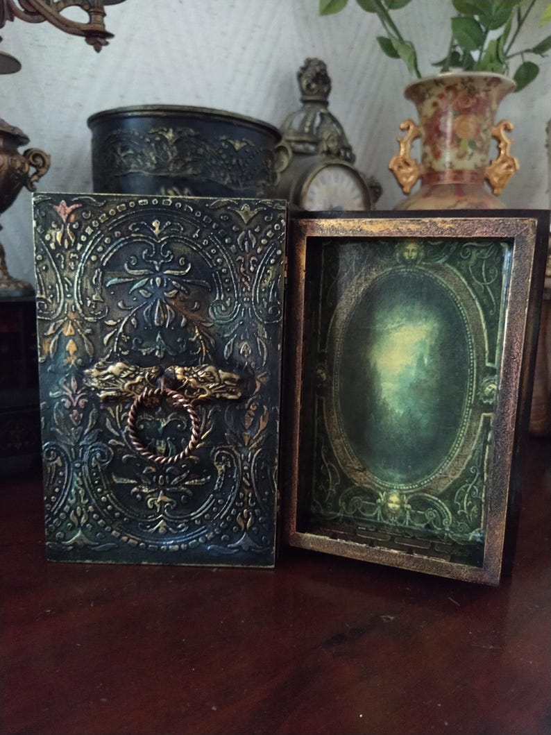 May include: A dark green wooden box with a gold-colored ornate design and a brass handle. The box is open, revealing a green and gold interior with a mirror.