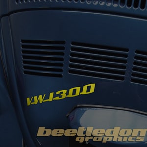 May include: A blue Volkswagen Beetle with a yellow "VW 1300" decal on the back. The car has a black grill and a chrome bumper. The text "beetledome graphics" is visible on the lower right side of the image.