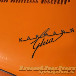 May include: A close-up of an orange car with a black "KARMANN Ghia" logo on the hood.