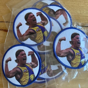 Puede incluir: Seis parches redondos con borde azul y fondo blanco que muestran una foto de un hombre flexionando los bíceps. El hombre lleva una camiseta amarilla y azul con la palabra "AFL" en ella.