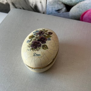 May include: A white egg-shaped trinket box with a floral design and the word "Daven" written on it.
