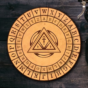 May include: A round, wooden cipher wheel with engraved letters and symbols. The outer ring features the alphabet, while the center displays a triangle with an ankh symbol. The wheel is light brown and sits on a dark wooden surface.