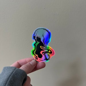 May include: A holographic sticker of a skull with a black and white design. The skull is melting and dripping with rainbow colors.