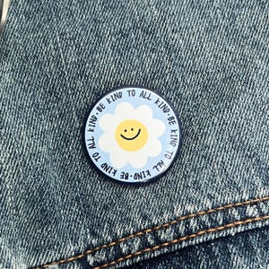 May include: A blue and white enamel pin with a daisy and the text "Be Kind To All Kind - Be Kind To All Kind".