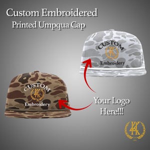 May include: Two custom embroidered Umpqua caps. One cap features a brown and tan camouflage pattern, the other a grey and white camouflage pattern. Both caps have a gold logo and the words "Custom Embroidery". The text "Your Logo Here!!!" is also visible.