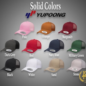 May include: A variety of solid color trucker hats with mesh back panels. The hats are arranged in two rows of five, with the brand name "YUPOONG" printed on the top of the image. The colors include pink, orange, burgundy, dark grey, red, navy blue, military green, black, white, sand, and stone.