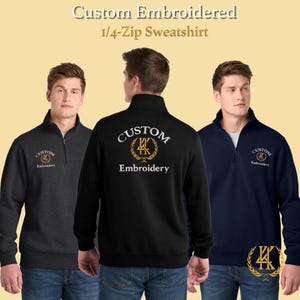 May include: Three custom embroidered 1/4-zip sweatshirts in charcoal, black, and navy blue. Each sweatshirt features the word "CUSTOM" above "Embroidery" with a gold emblem. The sweatshirts have a mock neck collar and a zipper.