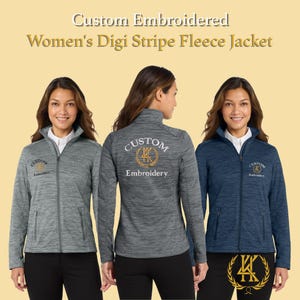 May include: Three women's Digi Stripe fleece jackets in gray and navy blue. Each jacket has a zip-up front, a high collar, and the word "Custom Embroidery" embroidered on the front and back. The jackets are displayed against a light yellow background.