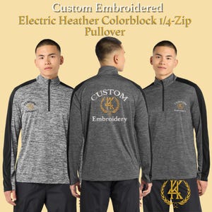 Peut inclure: Pull-over 1/4-zip électrique en colorblock chiné. La chemise à manches longues est grise avec des accents noirs sur les épaules et les manches. Le texte "Custom Embroidered" et "Embroidery" est visible sur la chemise.