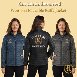 May include: Three packable puffer jackets in navy blue, black, and gray. Each jacket has a quilted design, a zipper closure, and the words "Custom Embroidery" embroidered on the front and back. The jackets are displayed on a light yellow background.
