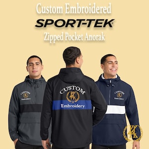 May include: Three custom embroidered Sport-Tek zipped pocket anoraks in the image. The anoraks are in black, navy, and gray. The text "Custom Embroidery" is embroidered on the front and back of the jackets. The jackets have a hood and a zipped pocket.