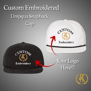 Op de afbeelding: Op maat geborduurde Umpqua snapback cap in zwart en wit. De caps hebben de tekst "CUSTOM Embroidery" in een goud en zwart ontwerp. De afbeelding bevat ook de tekst "Your Logo Here!!!".