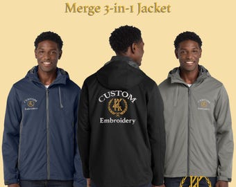 Può includere: Tre giacche Merge 3-in-1 ricamate su misura in blu navy, nero e grigio. Ogni giacca ha una chiusura con zip frontale, un cappuccio e il logo "Custom Embroidery". Le giacche sono esposte su uno sfondo giallo chiaro.