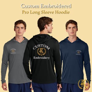 Op de afbeelding: Drie hoodies met lange mouwen in grijs, zwart en marineblauw worden getoond. Elke hoodie heeft een capuchon en een klein geborduurd logo op de borst. De zwarte hoodie heeft een groter geborduurd ontwerp op de rug met de woorden "Custom Embroidery".