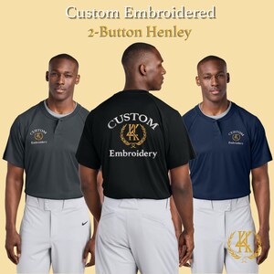 May include: Three men modeling custom embroidered 2-button Henley shirts. The shirts are in dark gray, black, and navy blue. The text "Custom Embroidery" is displayed on the front and back of the shirts. The shirts are paired with light gray baseball pants.