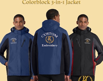 Può includere: Sono mostrate tre giacche 3 in 1 a blocchi di colore. Le giacche sono blu navy, nere e grigie. Ogni giacca ha un cappuccio e la scritta "Custom Embroidery" ricamata sul davanti e sul retro. Le giacche sono mostrate su uno sfondo giallo chiaro.