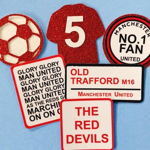 May include: A set of six red and white Manchester United themed stickers. The stickers feature a football, a jersey with the number 5, a sign that says "Old Trafford M16 Manchester United", a sign that says "The Red Devils", and two signs that say "Glory Glory Man United".