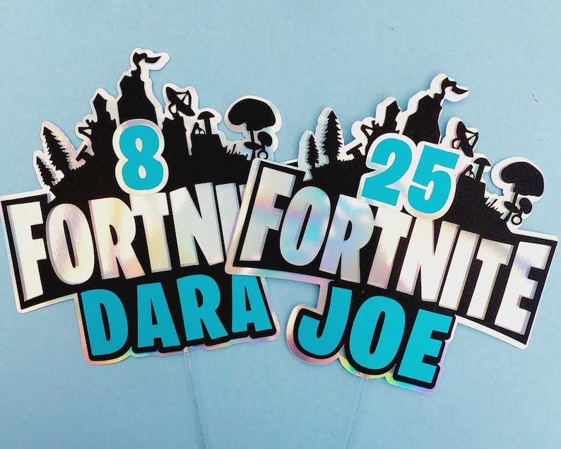 May include: Two Fortnite themed cake toppers with iridescent backgrounds. One topper says "Fortnite Dara 8" in blue and black lettering. The other topper says "Fortnite Joe 25" in blue and black lettering.