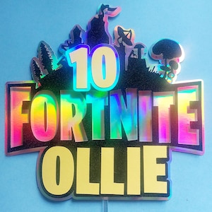 May include: A holographic cake topper with the words "10 Fortnite Ollie" in a rainbow color scheme. The topper features a silhouette of a Fortnite character and other game-related imagery.