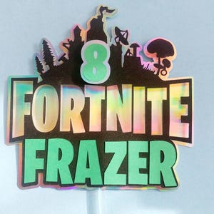 May include: A green and black cake topper with the words "Fortnite Frazer" and the number "8" in a green circle. The background is a black and iridescent design with a silhouette of a video game character.