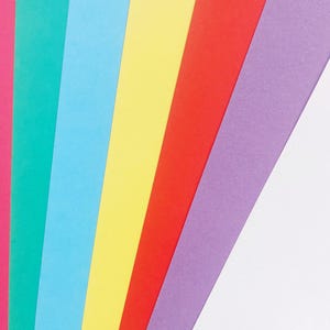 May include: A rainbow of colored paper strips arranged in a diagonal pattern. The colors are pink, teal, light blue, yellow, red, purple, and white.